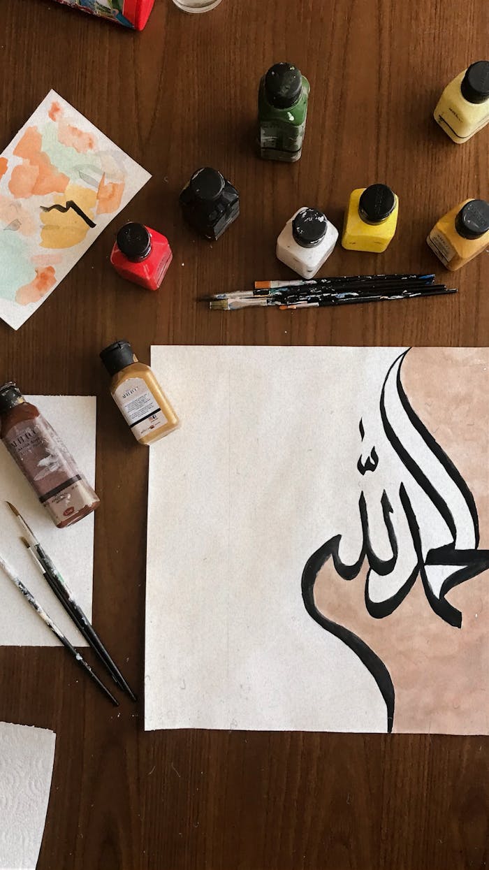 Overhead view of vivid paints and artistic Arabic calligraphy paper.